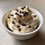 A white bowl filled with creamy Keto Chocolate Chip Cookie Dough Dip topped generously with mini chocolate chips.