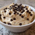 Close-up of creamy Keto Chocolate Chip Cookie Dough Dip topped generously with mini chocolate chips in a white bowl.