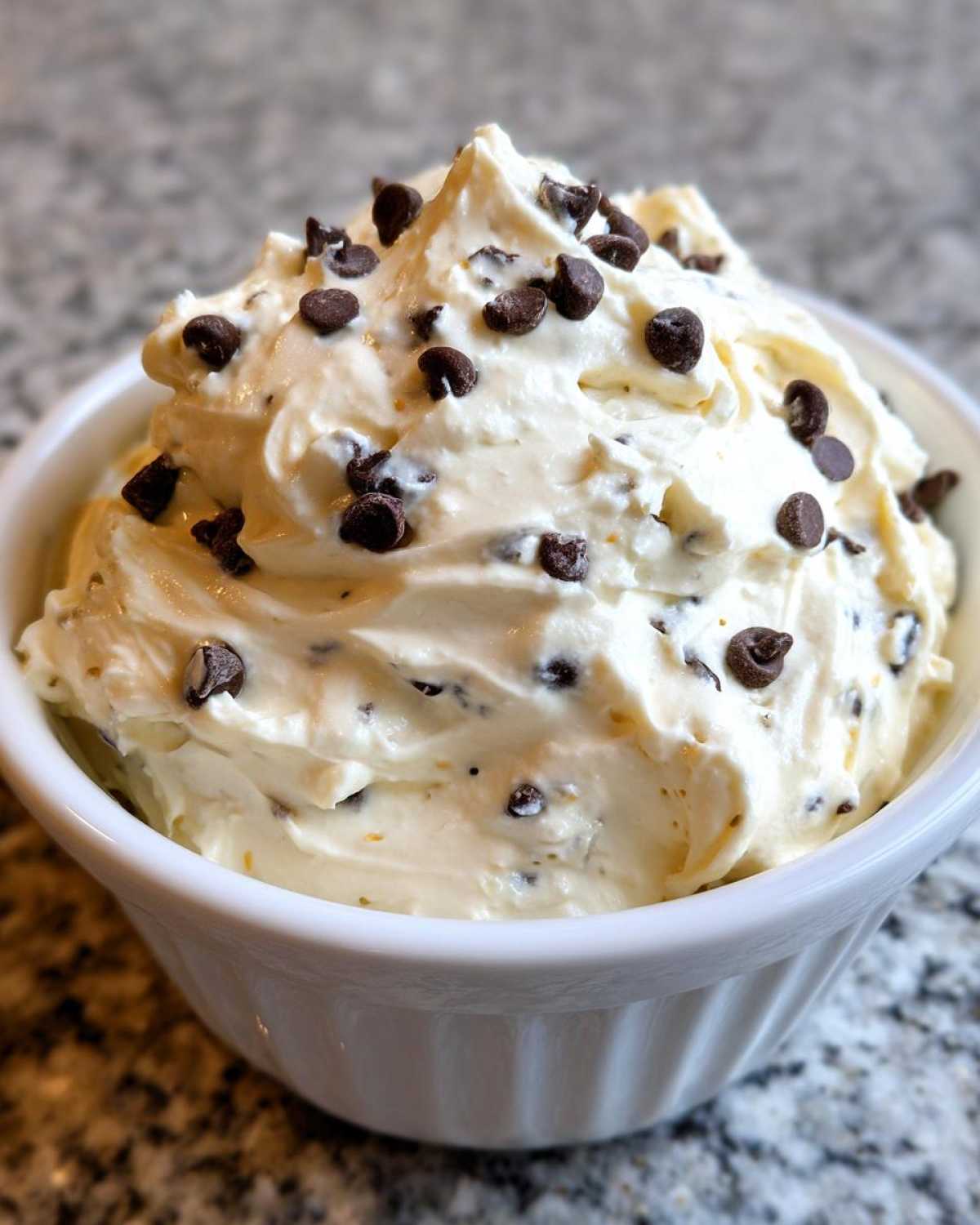 A close-up of creamy Keto Chocolate Chip Cookie Dough Dip topped with mini chocolate chips in a white ramekin.