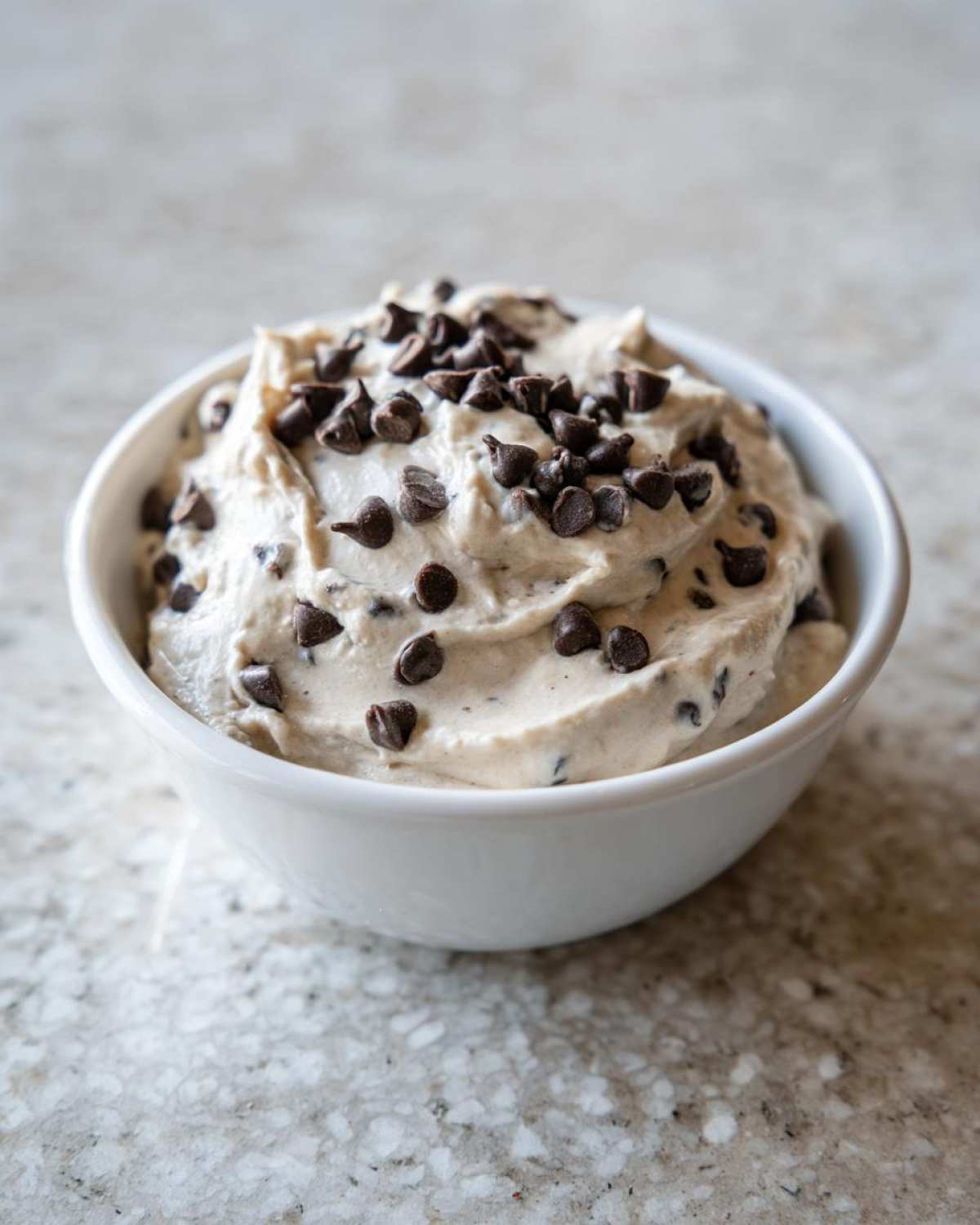 A white bowl filled with creamy Keto Chocolate Chip Cookie Dough Dip, topped generously with mini chocolate chips.