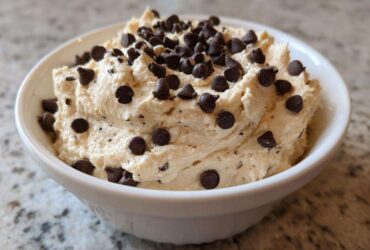 Close-up of creamy Keto Chocolate Chip Cookie Dough Dip topped generously with mini chocolate chips in a white bowl.
