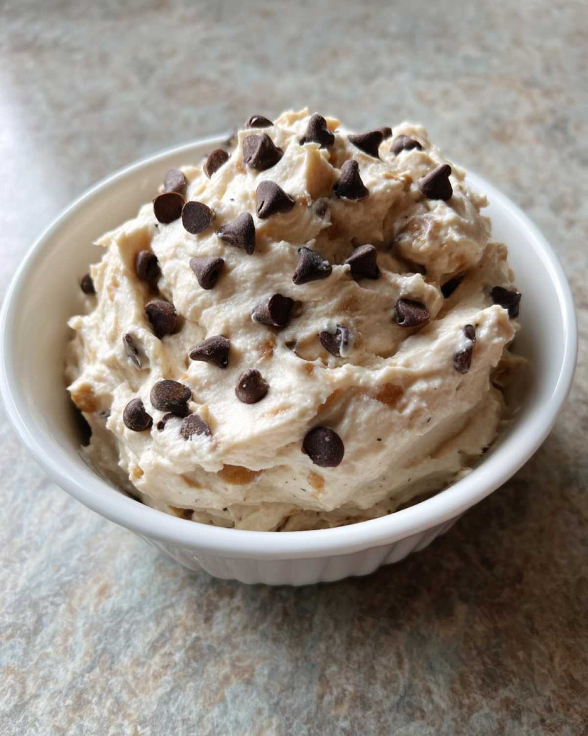 A white bowl filled with creamy Keto Chocolate Chip Cookie Dough Dip topped generously with mini chocolate chips.