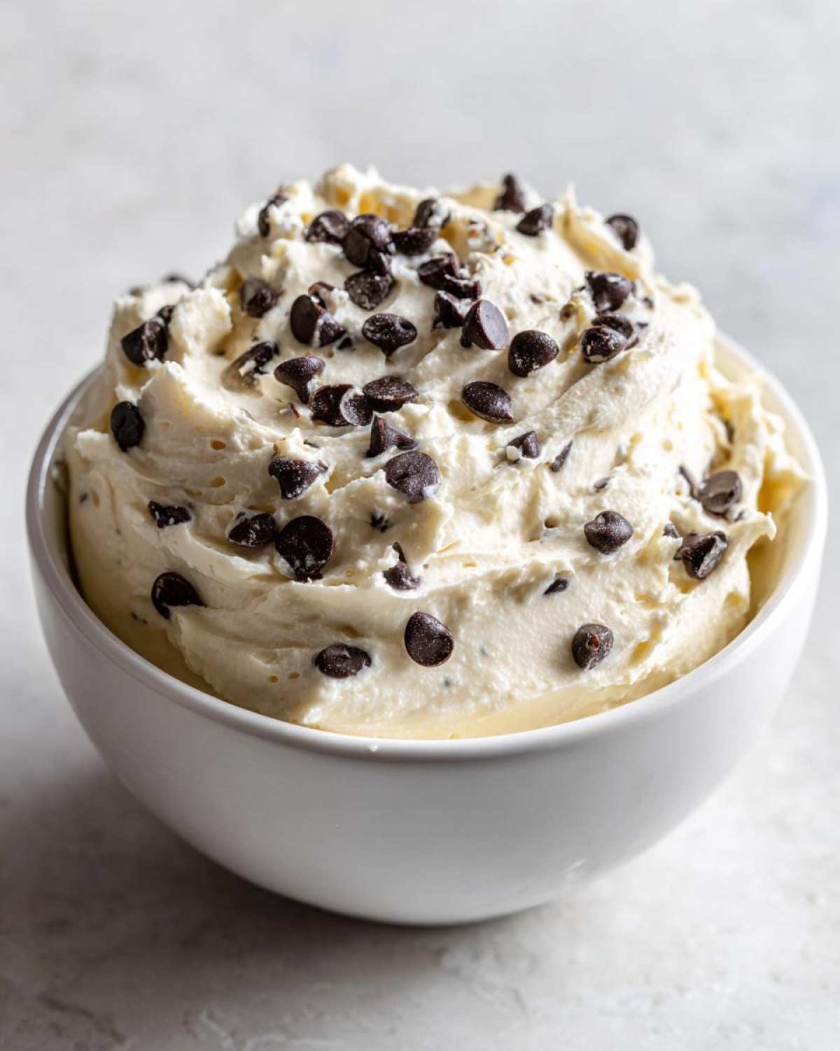 A white bowl filled with fluffy Keto Chocolate Chip Cookie Dough Dip topped generously with mini chocolate chips.