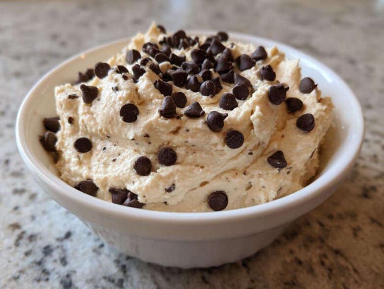 Close-up of creamy Keto Chocolate Chip Cookie Dough Dip topped generously with mini chocolate chips in a white bowl.