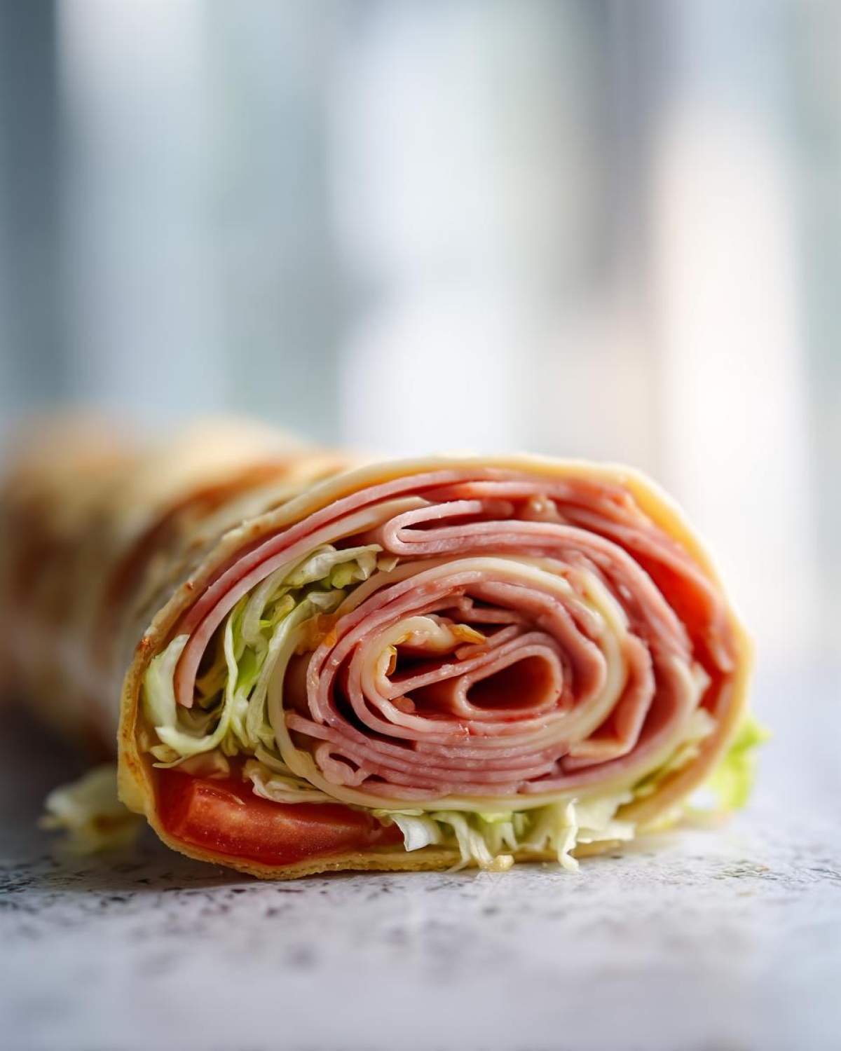 Cross-section view of a tightly rolled Keto Italian Sub Roll-Ups showing layers of deli meat, cheese, lettuce, and tomato.