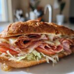 A delicious-looking Keto Italian Sub Roll-Ups sandwich filled with melted cheese, deli meats, lettuce, and tomato, served on a white plate.