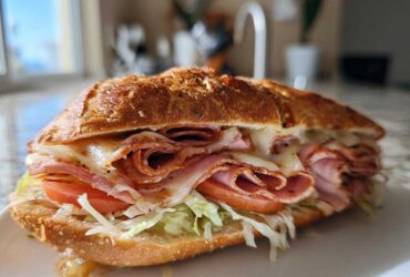 A delicious-looking Keto Italian Sub Roll-Ups sandwich filled with melted cheese, deli meats, lettuce, and tomato, served on a white plate.
