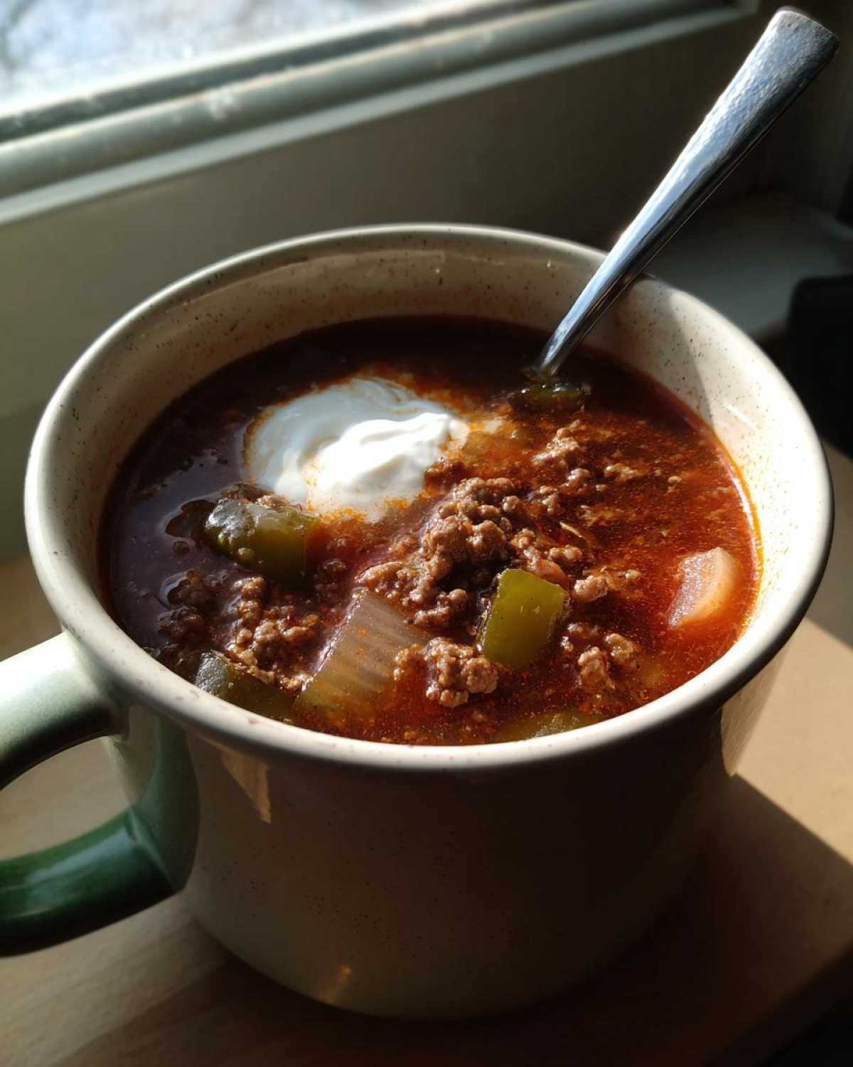 Close-up of a hearty serving of Keto Taco Soup with Ground Beef topped with sour cream in a speckled mug.