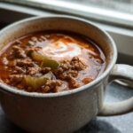 Close-up of a hearty serving of Keto Taco Soup with Ground Beef topped with sour cream in a speckled mug.