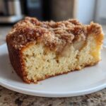A close-up of a moist slice of apple crumb cake showing the tender cake base, baked apple pieces, and rich cinnamon streusel topping.