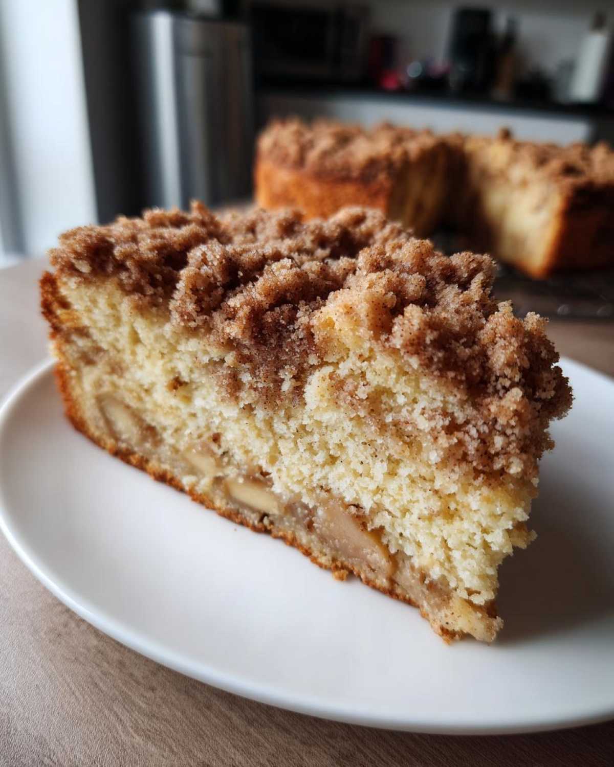 Close-up of a moist slice of apple crumb cake showing tender cake, baked apple pieces, and a thick cinnamon streusel topping.