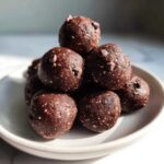 A stack of rich, dark No-Bake Brownie Batter Protein Balls topped with mini chocolate chips on a light gray plate.
