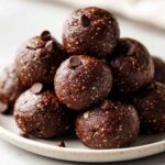 A close-up stack of rich, dark No-Bake Brownie Batter Protein Balls topped with mini chocolate chips.