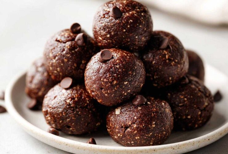 A close-up stack of rich, dark No-Bake Brownie Batter Protein Balls topped with mini chocolate chips.