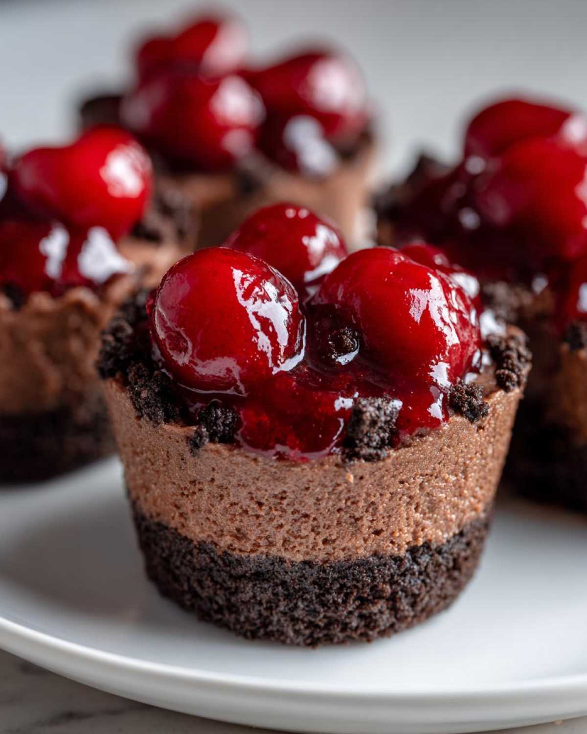 A close-up of one of the No-Bake Chocolate Cherry Cheesecake Cups, featuring a dark crust, chocolate filling, and bright cherry topping.