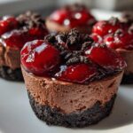 A close-up of individual No-Bake Chocolate Cherry Cheesecake Cups topped with glossy cherries and cookie crumbs.