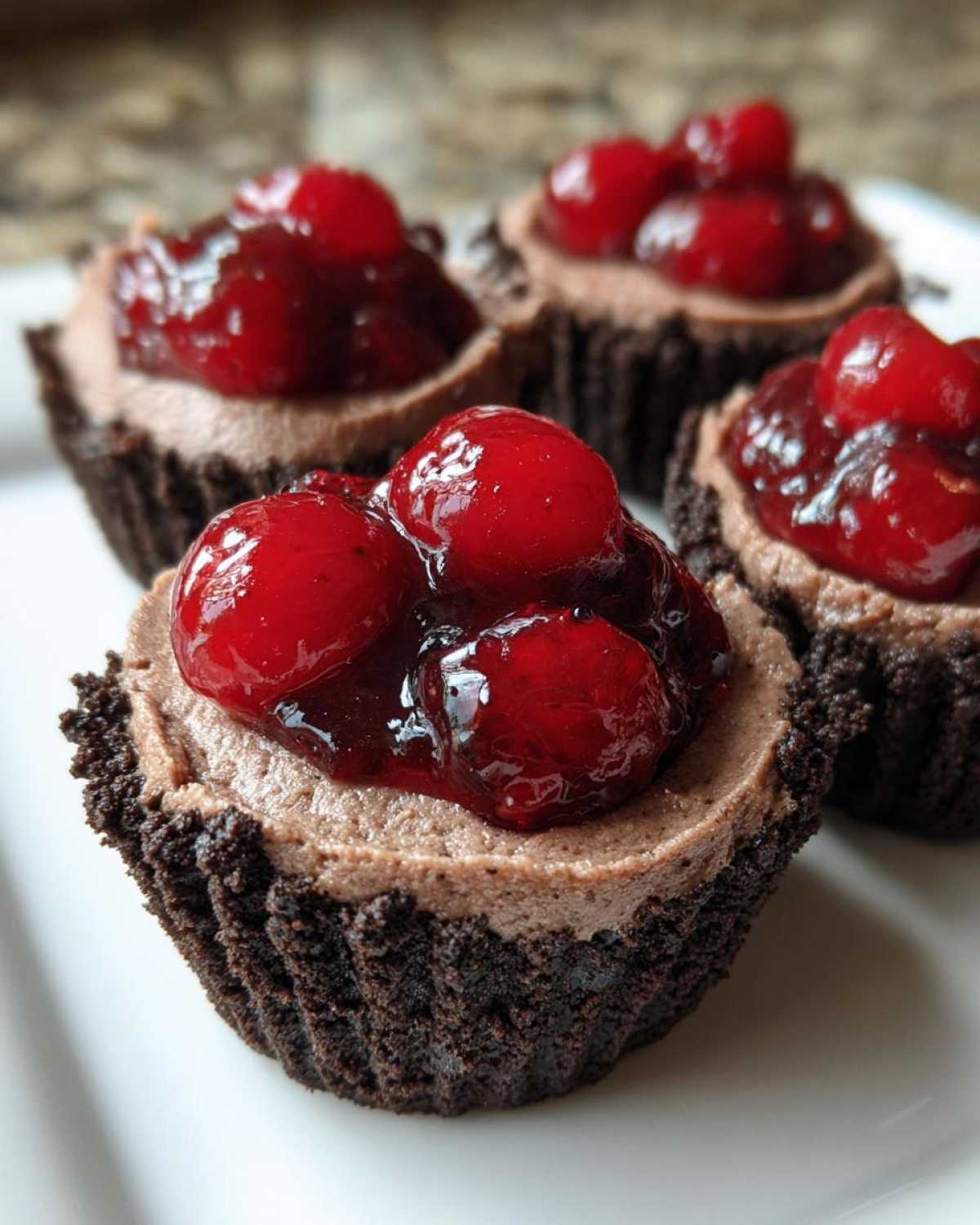 Four No-Bake Chocolate Cherry Cheesecake Cups with chocolate crust and cherry topping.