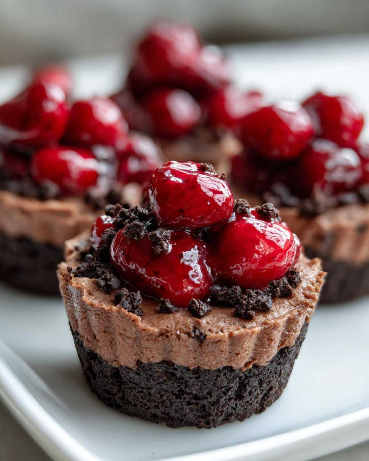 A close-up of a No-Bake Chocolate Cherry Cheesecake Cup topped with glossy cherries and cookie crumbs.