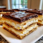 Close-up of a layered slice of No-Bake Chocolate Eclair Cake with graham crackers, cream filling, and chocolate frosting.