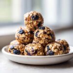 A stack of delicious No-Bake Lemon Blueberry Energy Bites made with oats and dried blueberries on a small white plate.