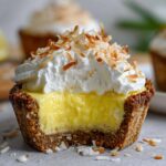 A bite taken out of a No-Bake Lemon Coconut Cream Pie Cup showing the bright yellow filling and toasted coconut topping.