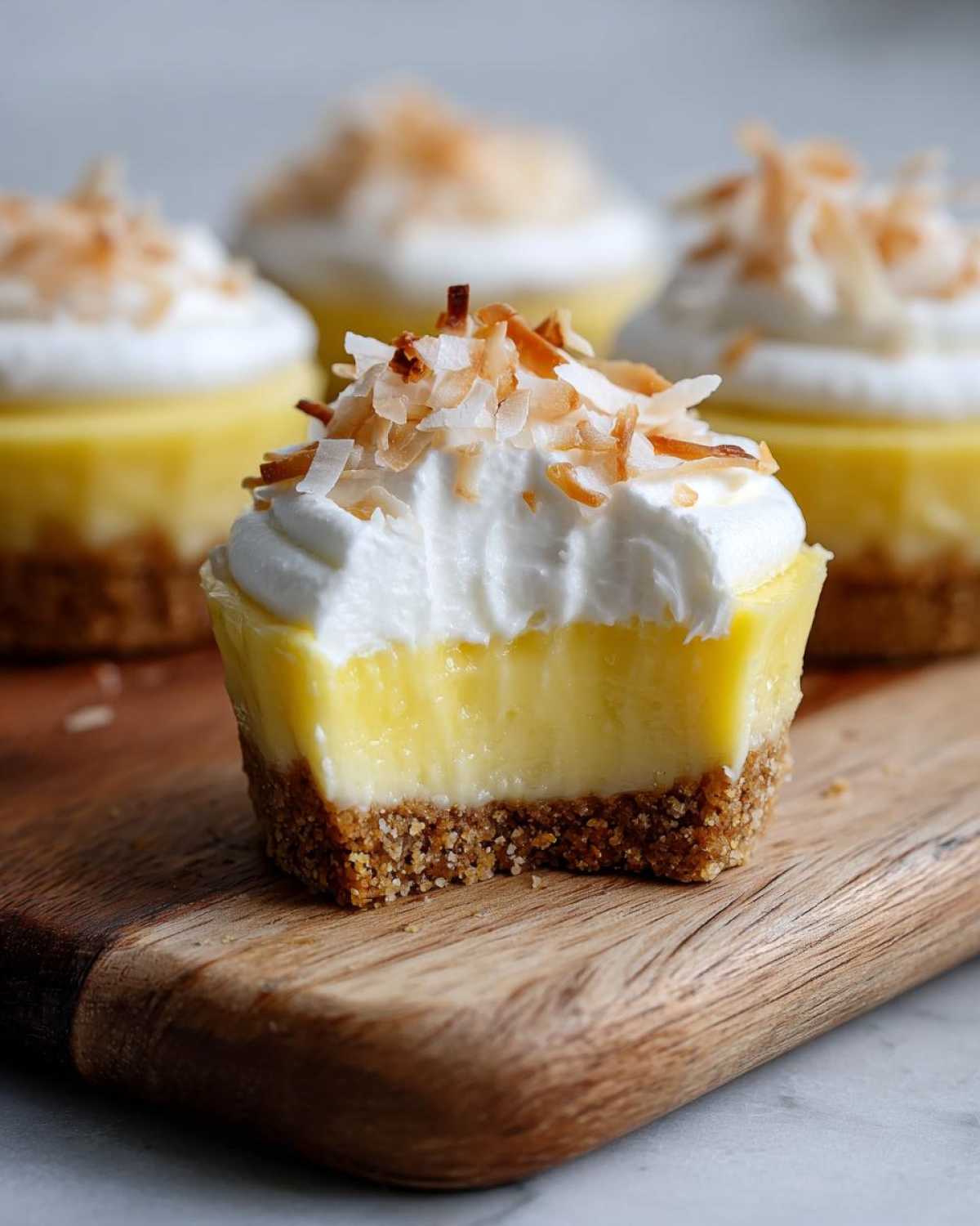 A close-up of a No-Bake Lemon Coconut Cream Pie Cup with a bite taken out, showing graham cracker crust, lemon filling, and whipped topping.