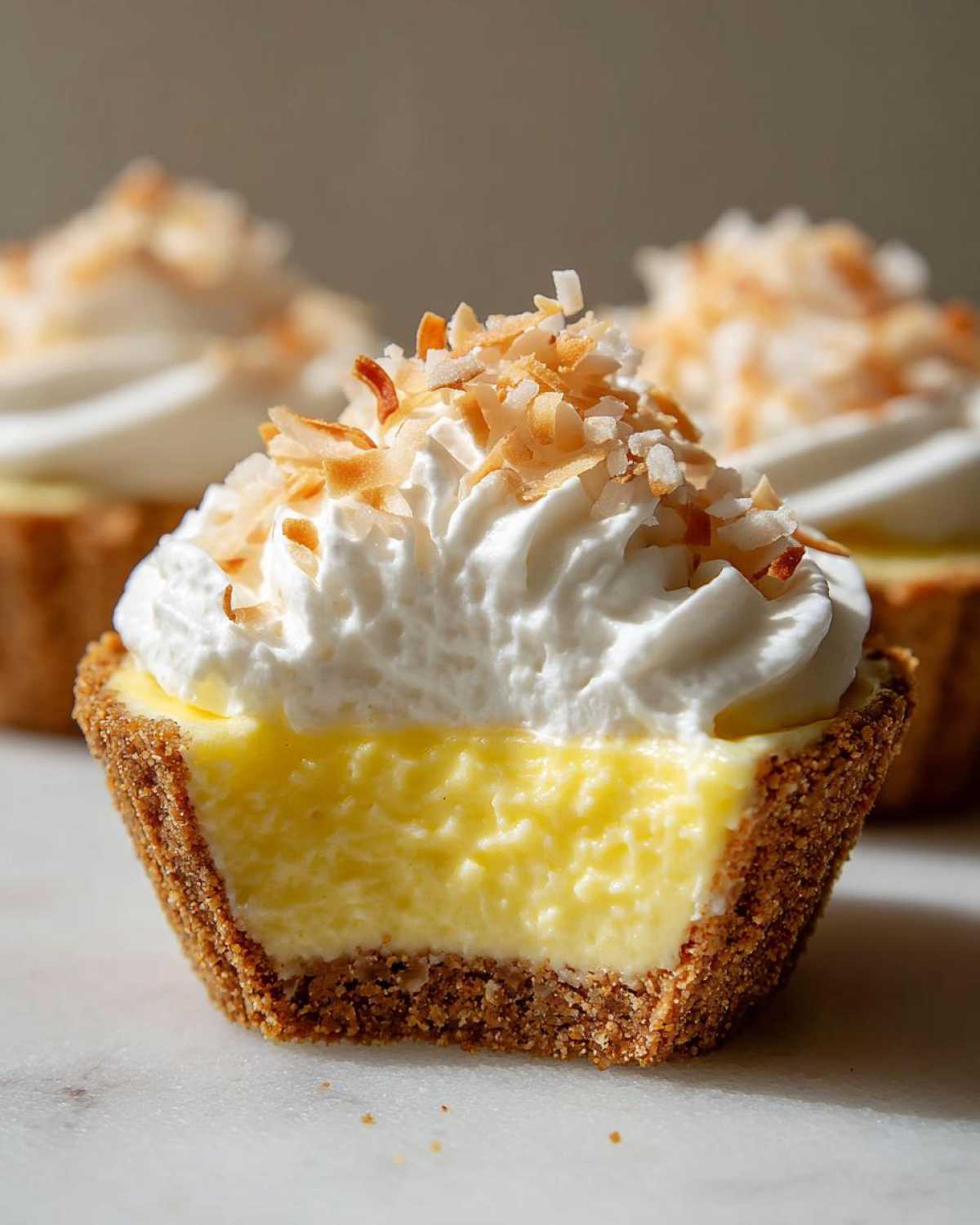 Close-up of a No-Bake Lemon Coconut Cream Pie Cup cut in half showing the crust, lemon filling, and whipped topping with toasted coconut.