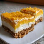 Two layered No-Bake Orange Creamsicle Cheesecake Bars resting on a white plate.