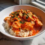 Close-up of One-Pot Creamy Tomato Basil Chicken and Rice served over white rice in a white bowl.