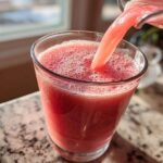 Close-up of a bright pink watermelon smoothie being poured from a blender pitcher into a glass.