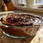 A close-up of rich, dark chocolate mousse topped with chocolate shavings in a clear glass bowl.
