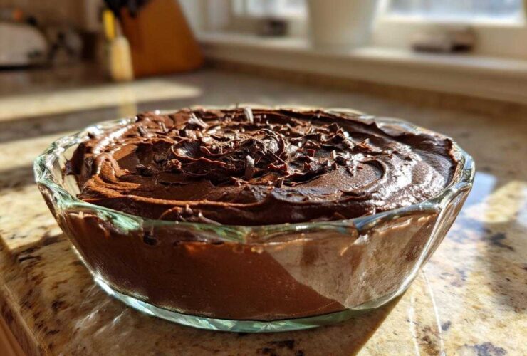 A close-up of rich, dark chocolate mousse topped with chocolate shavings in a clear glass bowl.