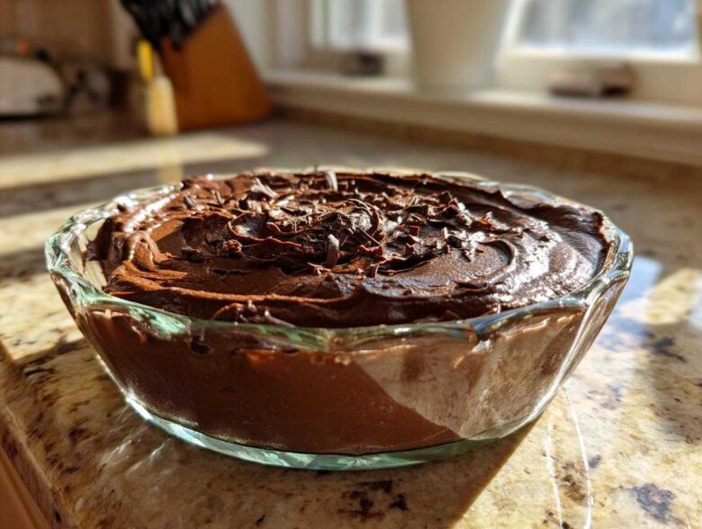 A close-up of rich, dark chocolate mousse topped with chocolate shavings in a clear glass bowl.