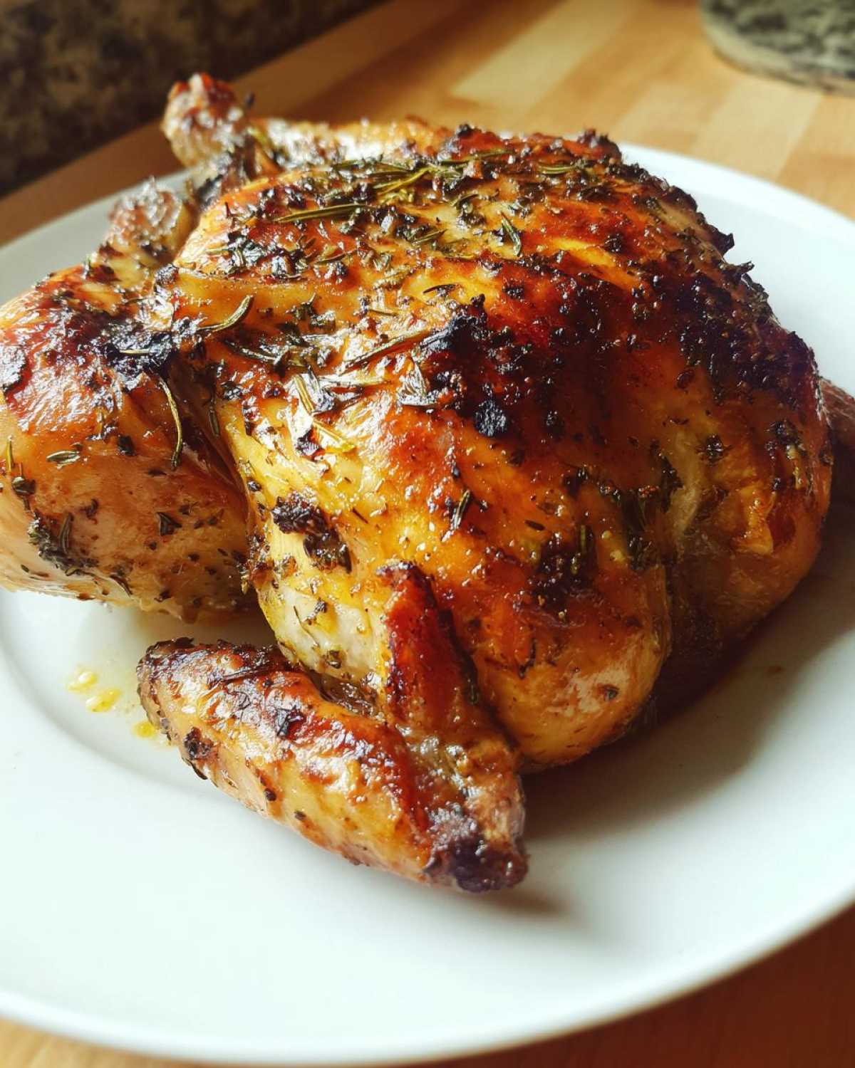 A beautifully roasted spatchcock chicken with crispy, golden-brown skin seasoned with herbs, resting on a white plate.