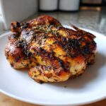 A beautifully roasted spatchcock chicken with crispy, herb-crusted skin resting on a white plate.