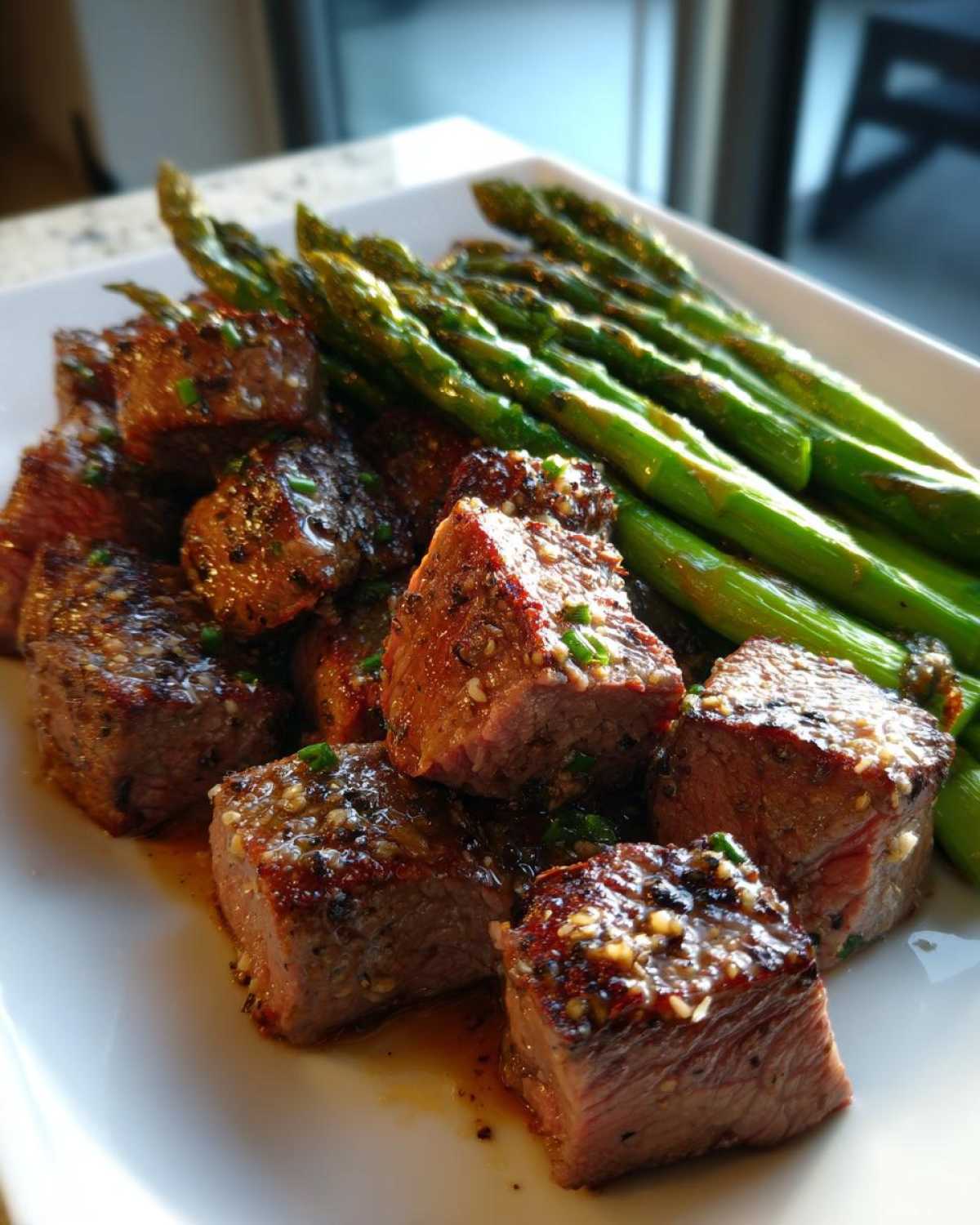 Close-up of juicy steak bites coated in garlic butter next to bright green asparagus spears.