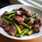 Close-up of juicy steak bites and bright green asparagus tossed in garlic butter sauce for Sheet Pan Garlic Butter Steak and Asparagus.