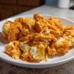 Close-up of shredded chicken mixed with creamy white cheese and bright orange buffalo sauce, ready for buffalo chicken recipes.