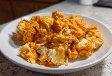 Close-up of shredded chicken mixed with creamy white cheese and bright orange buffalo sauce, ready for buffalo chicken recipes.