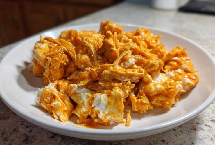 Close-up of shredded chicken mixed with creamy white cheese and bright orange buffalo sauce, ready for buffalo chicken recipes.