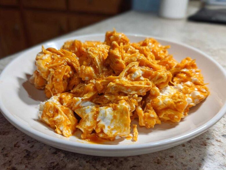 Close-up of shredded chicken mixed with creamy white cheese and bright orange buffalo sauce, ready for buffalo chicken recipes.
