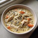 A close-up of a bowl filled with rich Slow Cooker Creamy Chicken and Wild Rice Soup, featuring shredded chicken, wild rice, and carrots.