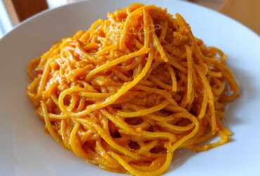Close-up of spaghetti noodles fully coated in a vibrant orange butternut squash pasta sauce on a white plate.