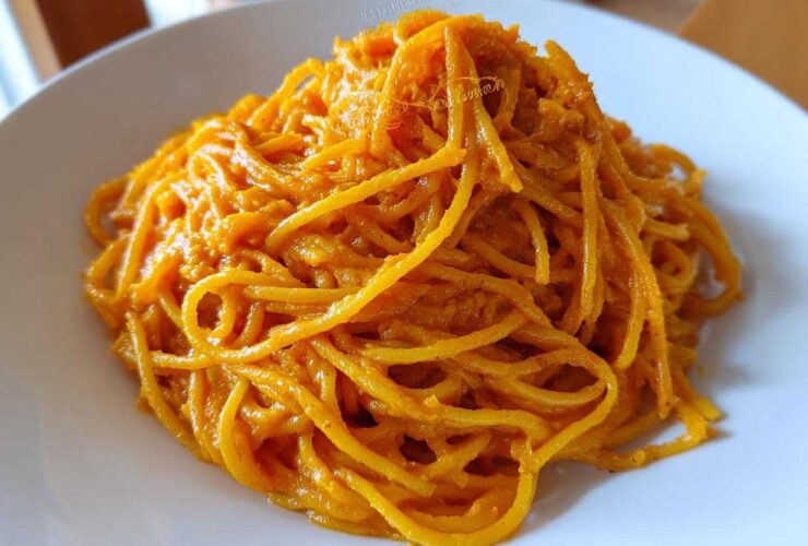 Close-up of spaghetti noodles fully coated in a vibrant orange butternut squash pasta sauce on a white plate.