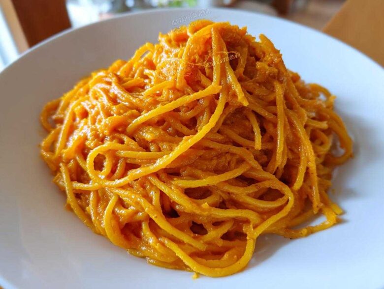 Close-up of spaghetti noodles fully coated in a vibrant orange butternut squash pasta sauce on a white plate.