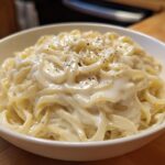 A white bowl filled with fettuccine pasta generously coated in Vegan Creamy Cashew Alfredo Sauce and topped with black pepper.