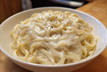 A white bowl filled with fettuccine pasta generously coated in Vegan Creamy Cashew Alfredo Sauce and topped with black pepper.