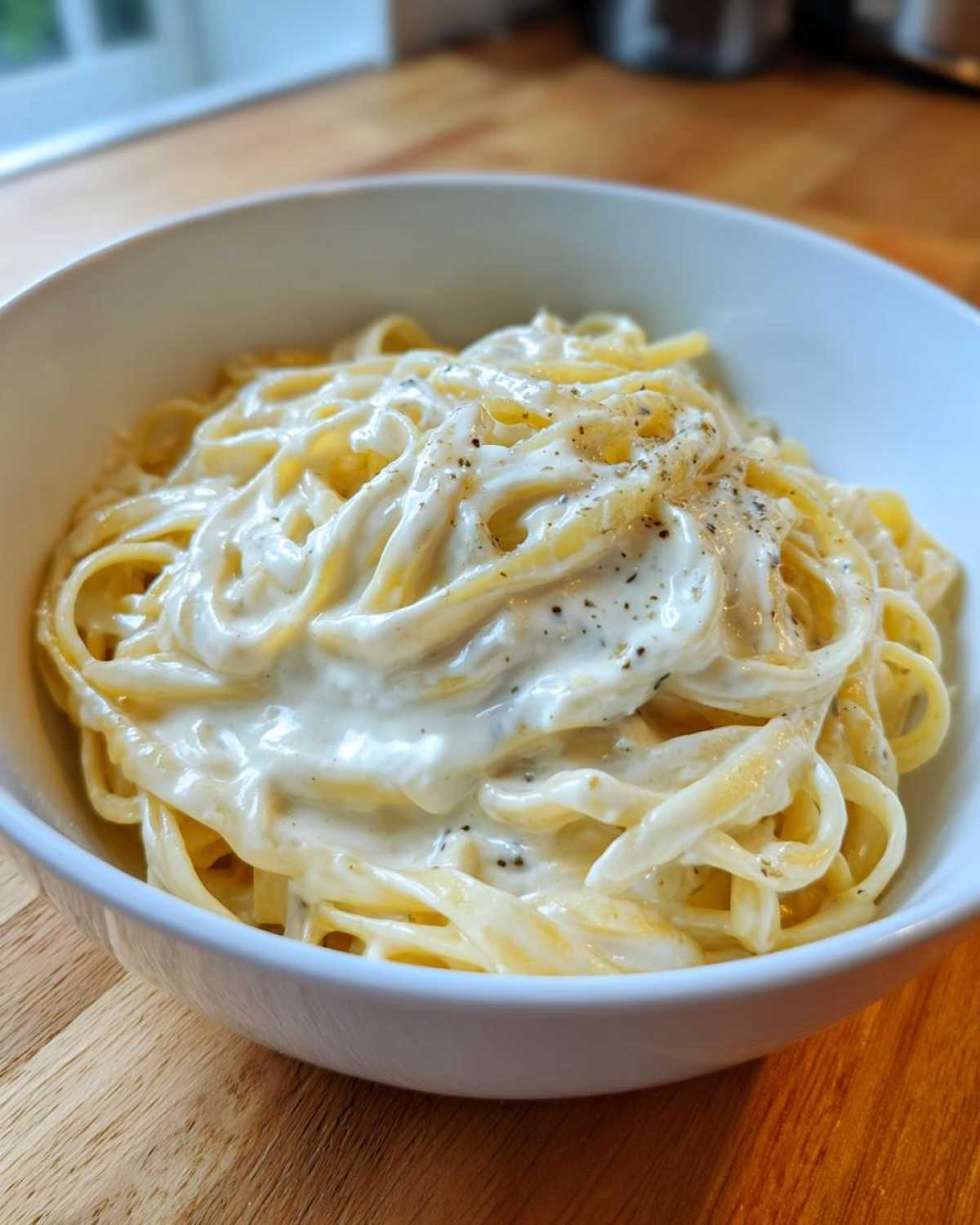 A white bowl filled with fettuccine pasta generously coated in Vegan Creamy Cashew Alfredo Sauce and topped with black pepper.
