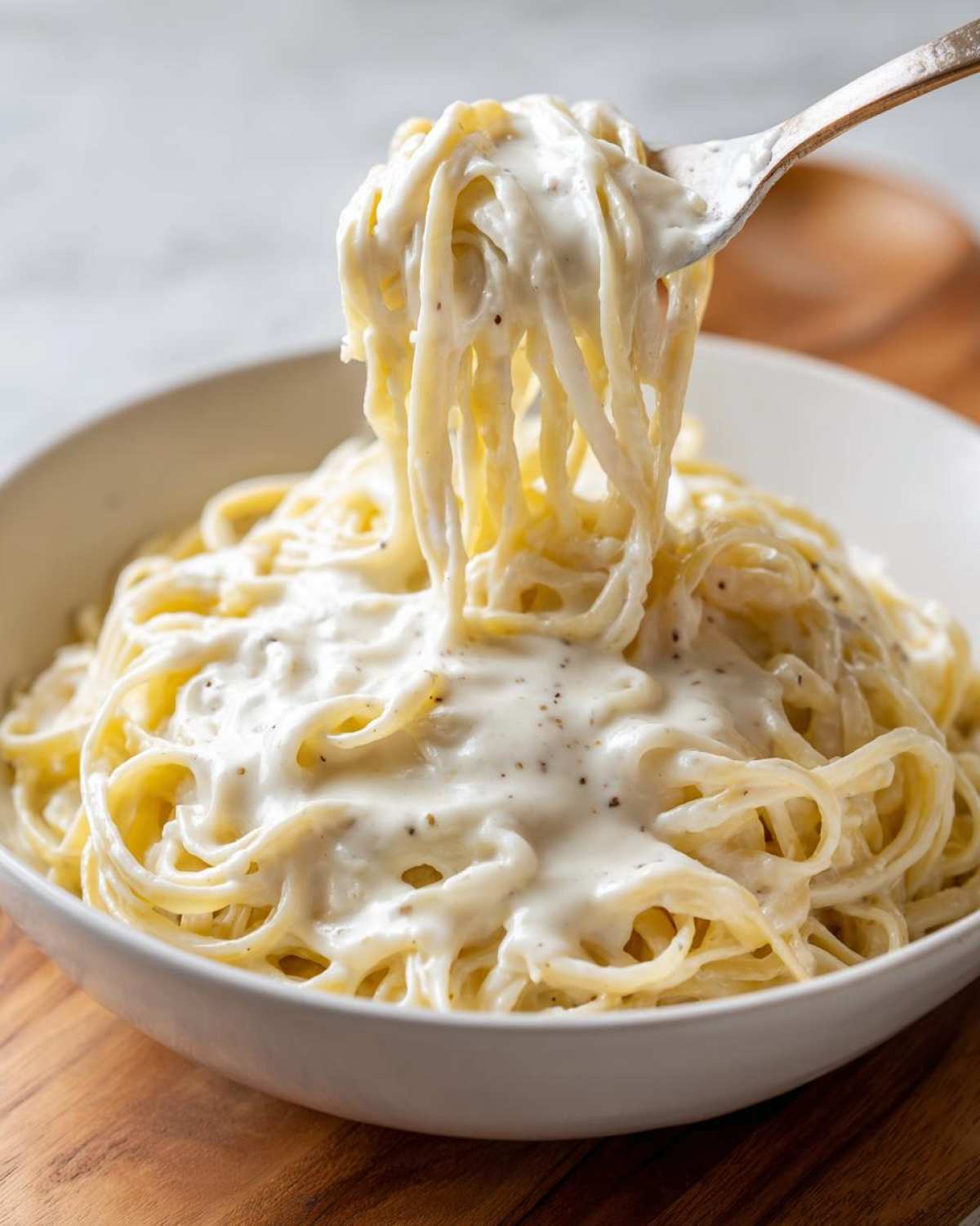 A fork lifting spaghetti generously coated in rich Vegan Creamy Cashew Alfredo Sauce from a white bowl.