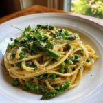 A close-up of creamy Vegan Lemon Asparagus Pasta mixed with bright green peas and topped with fresh pea shoots.